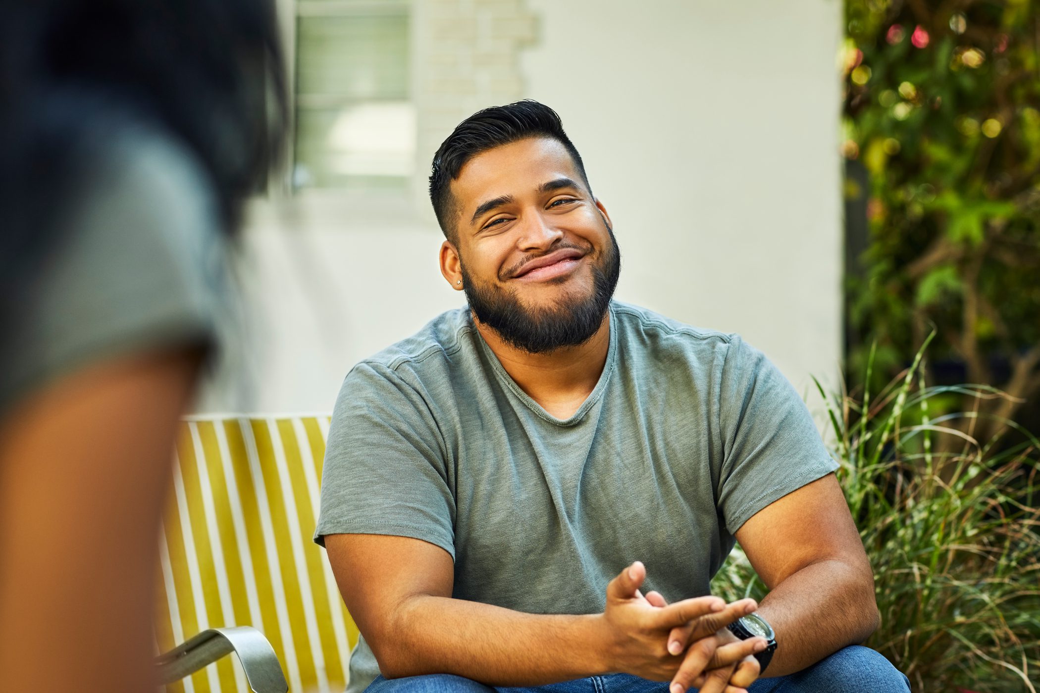 A man smiles broadly while sitting outdoors with an unseen woman.