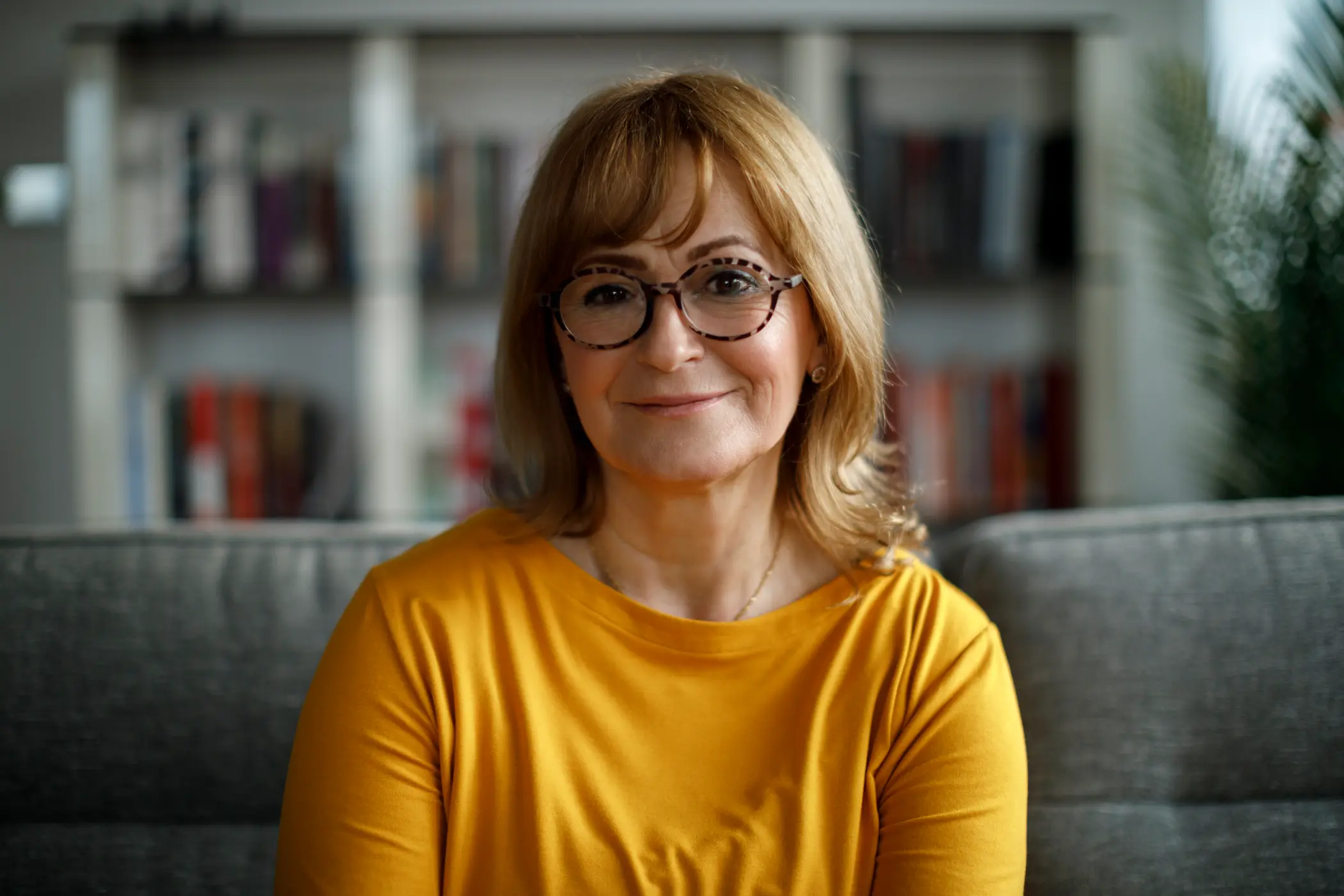 A mature woman sits in an office and smiles at the camera.