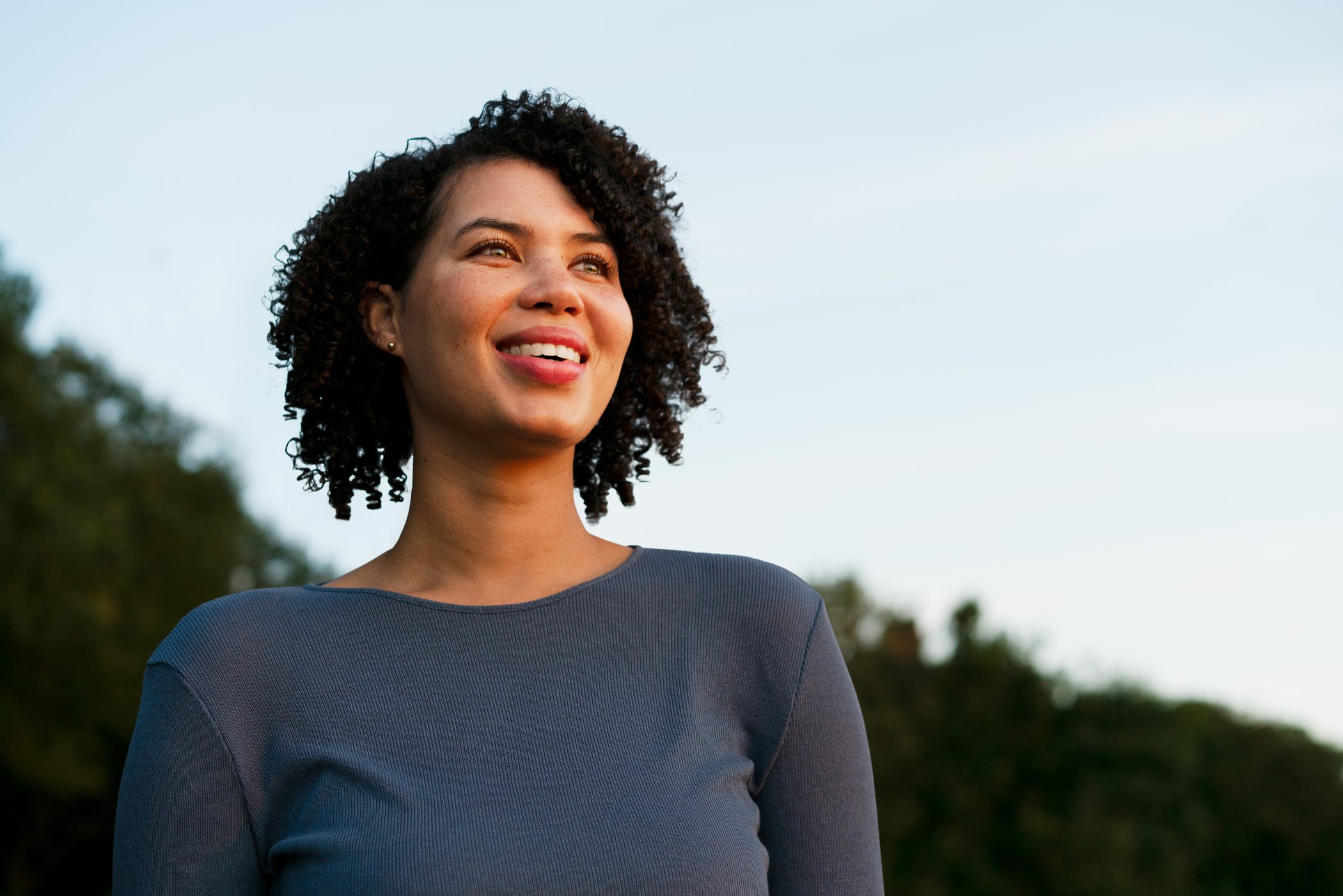 An African American woman looks off into the sky, hopeful.