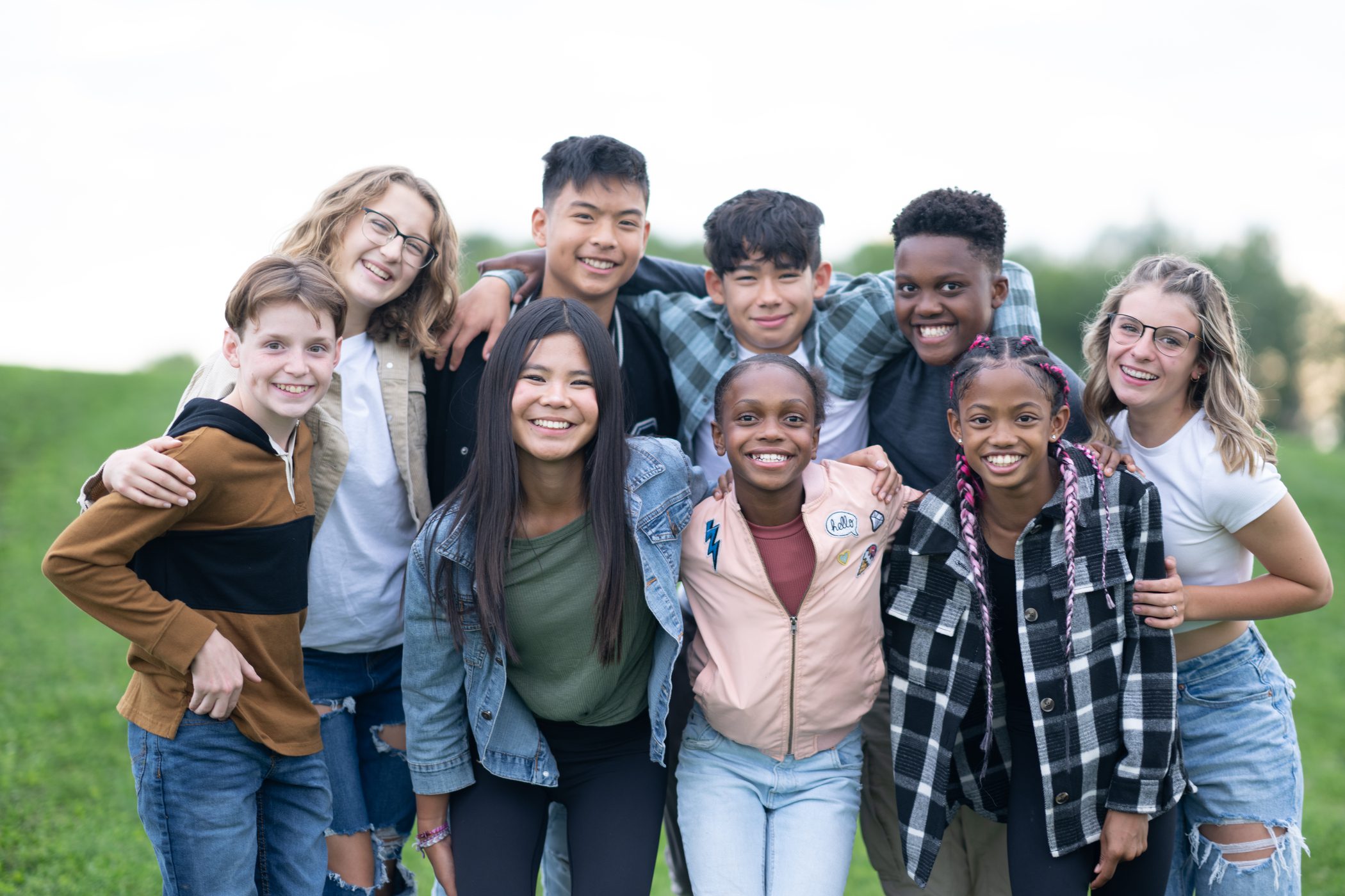 A group of children and adolescents hold each other shoulder to should as they smile for a picture.