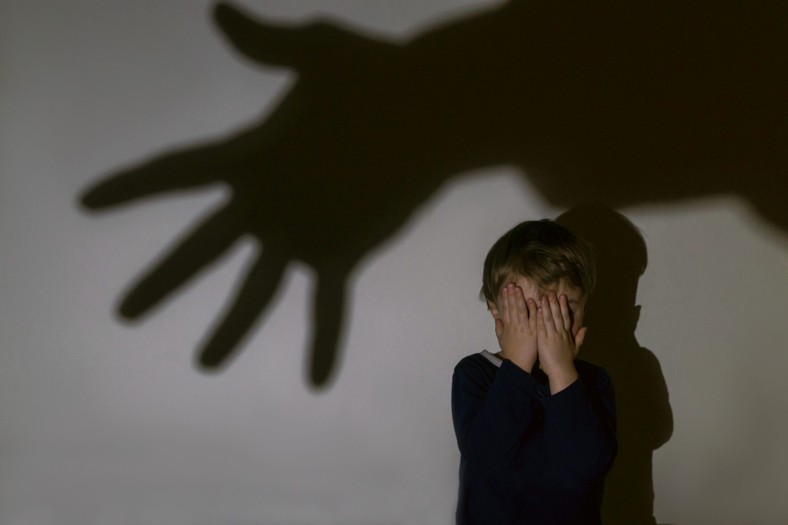 Little boy covers his eyes in fear as a shadow of a big hand looms over him.